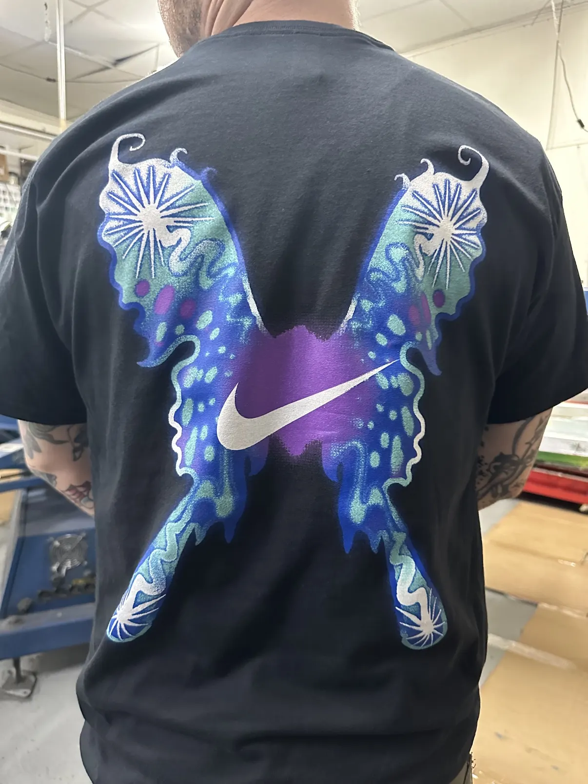 Black tee worn in the shop with a large multi-color butterfly back print built around the Nike swoosh