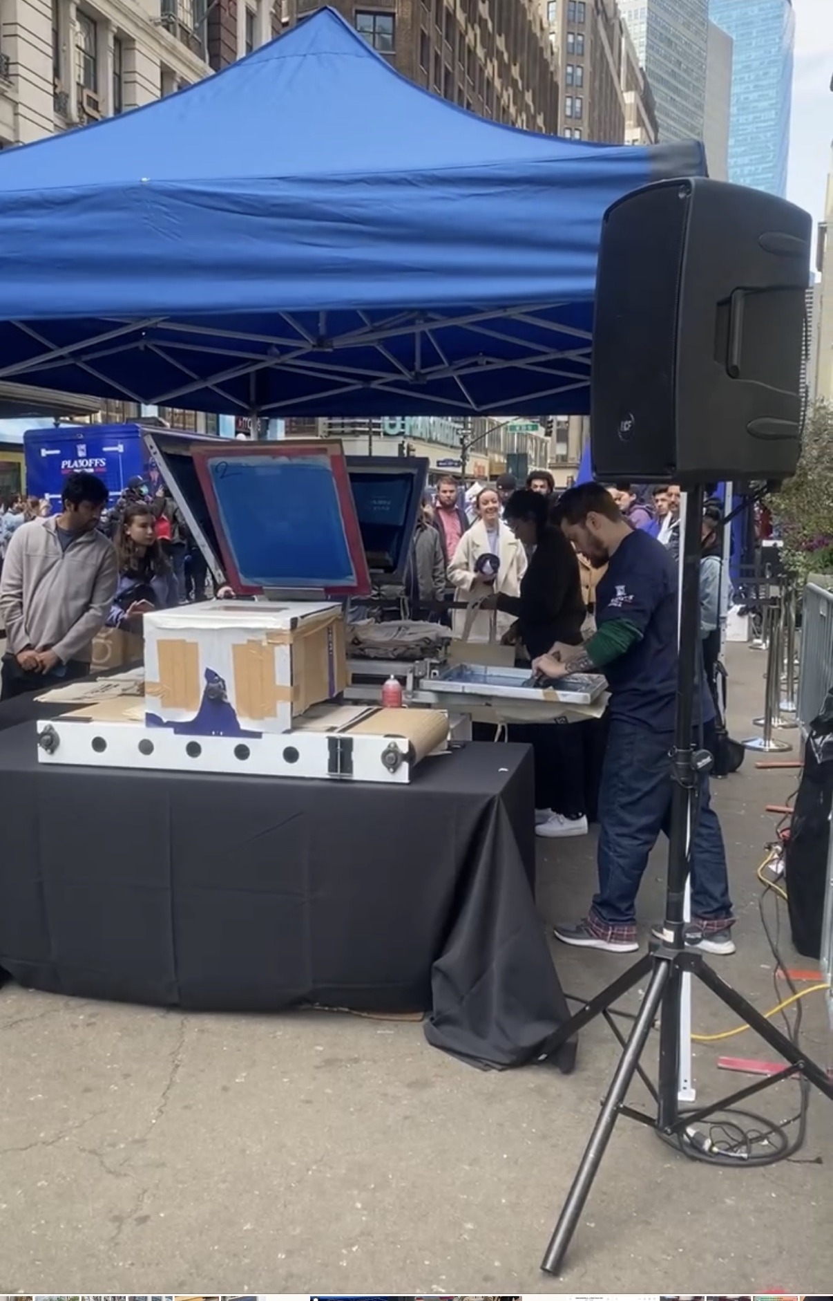 Live printing tent setup with press and dryer on the street at Herald Square, guests watching